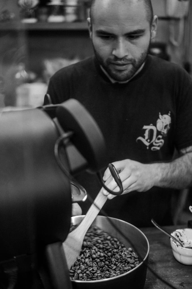 A person roasting coffee beans, stirring them in a large roaster